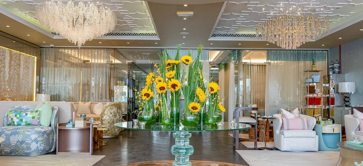 Sunflower arrangement in a tall green glass vase in a furnished interior.