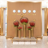 Wide view of The Royal Ornament installation in the First Class Lounge, featuring gold pedestal spheres crafted from woven Salix and filled with red Ilex and Amaryllis beneath world time clocks