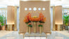 Luxury lobby floral installation with orange Ilex berries, copper asparagus, and amaryllis arranged on tall gold cylinders in a modern interior with world clocks.