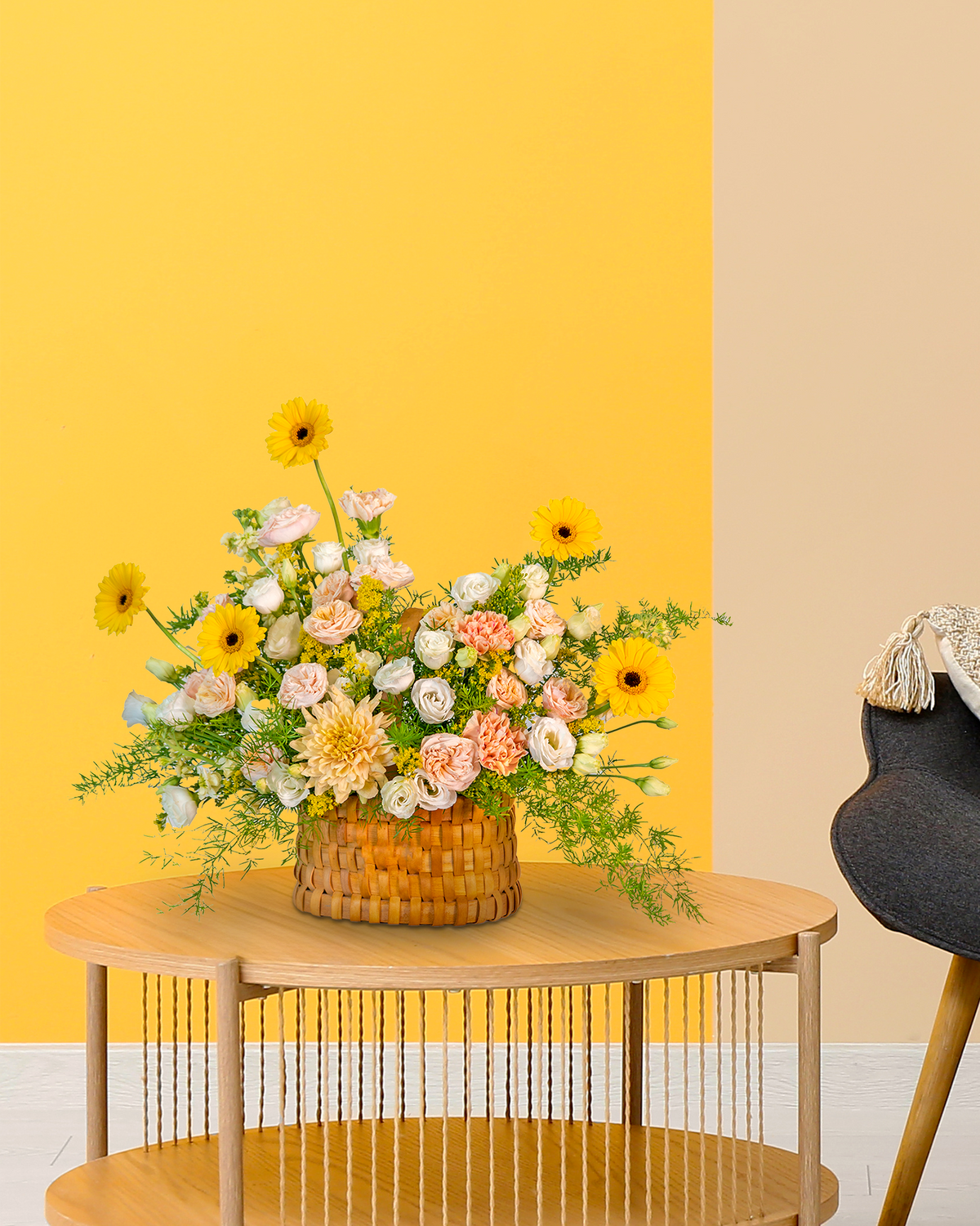 Floral arrangement in a woven basket on a wooden table against a yellow wall.