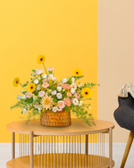 Floral arrangement in a woven basket on a wooden table against a yellow wall.