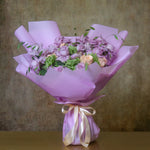 A bouquet of purple flowers including roses, orchids, and chrysanthemums, wrapped in purple paper with a golden ribbon.