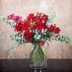 Glass vase arrangement of red roses, orchids, red berries, and eucalyptus foliage styled in a romantic design.