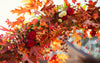 Vibrant autumn floral arrangement featuring red roses, orange spray roses, chrysanthemums, and oak leaves in warm fall tones, capturing the beauty of seasonal blooms.