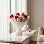 Bouquet of red and pink flowers in a white vase on a marble table.