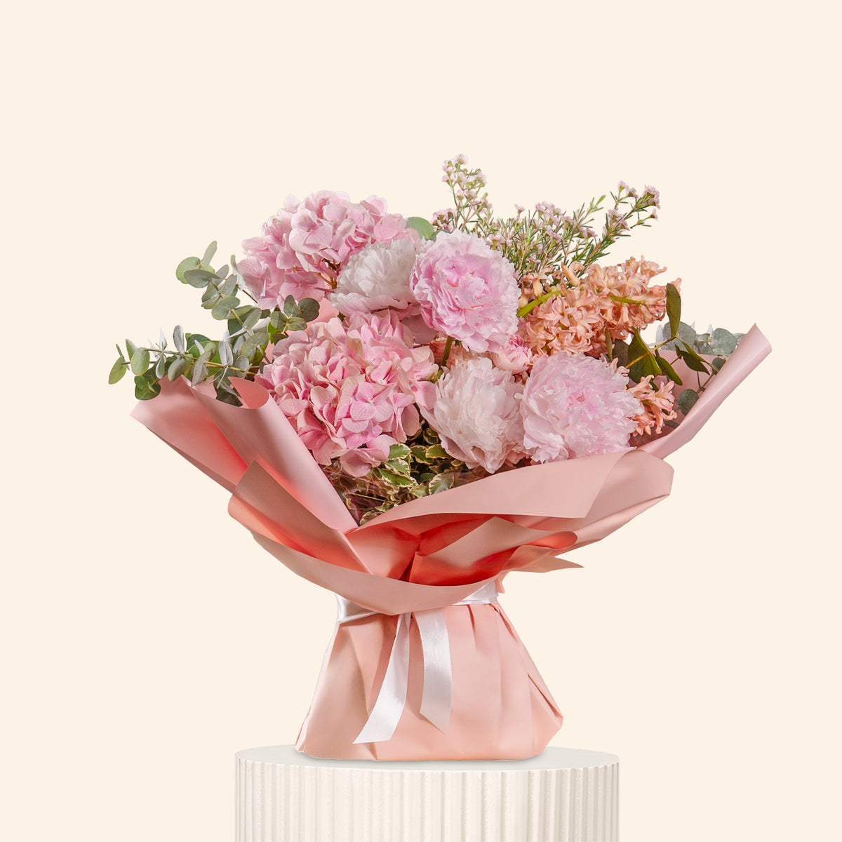 Bouquet of pink flowers with greenery on a white pedestal against a light beige background