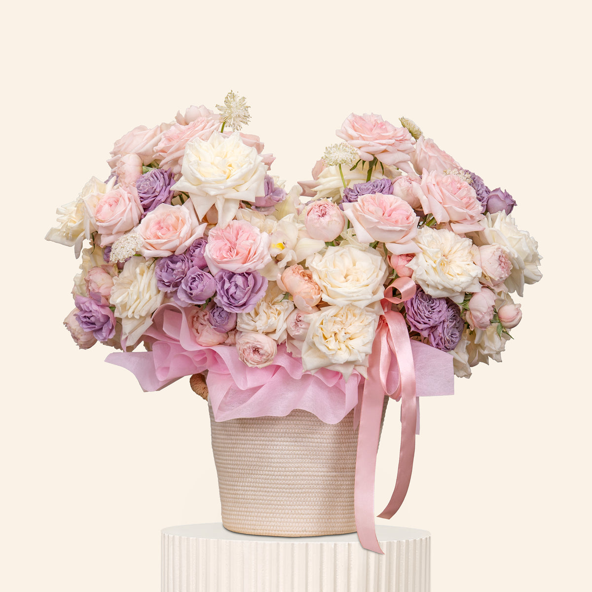 Bouquet of pink and white flowers with a pink ribbon in a white container on a light beige background