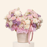Bouquet of pink and white flowers with a pink ribbon in a white container on a light beige background
