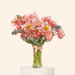 Bouquet of pink flowers in a clear vase on a white pedestal with a light beige background