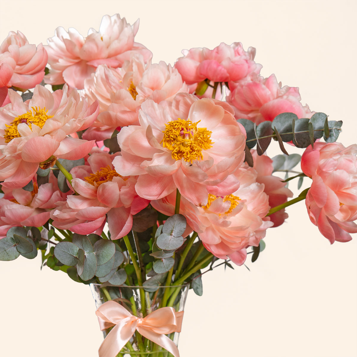 Bouquet of pink flowers with green leaves in a clear vase on a light background