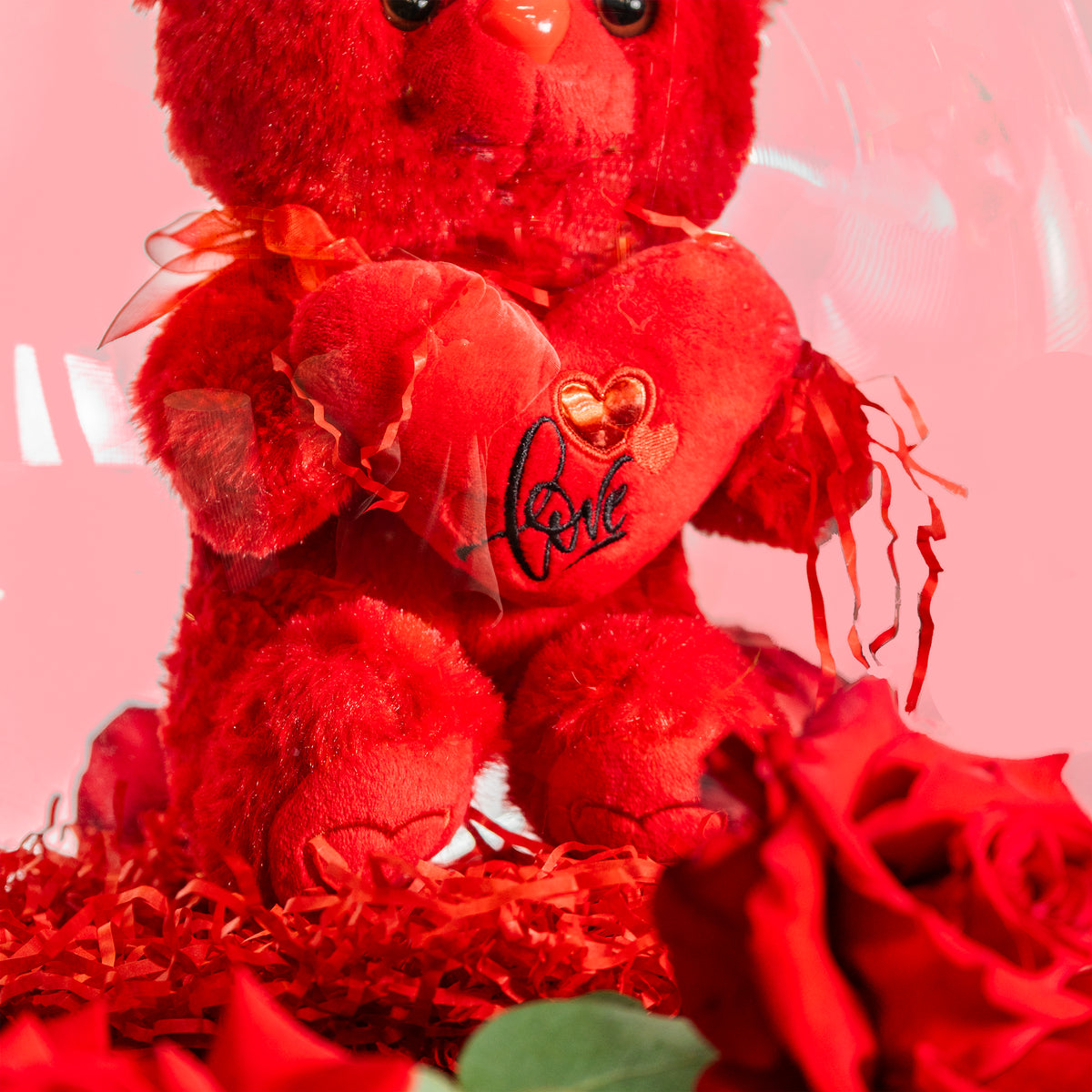 Red teddy bear with a heart and roses on a pink background