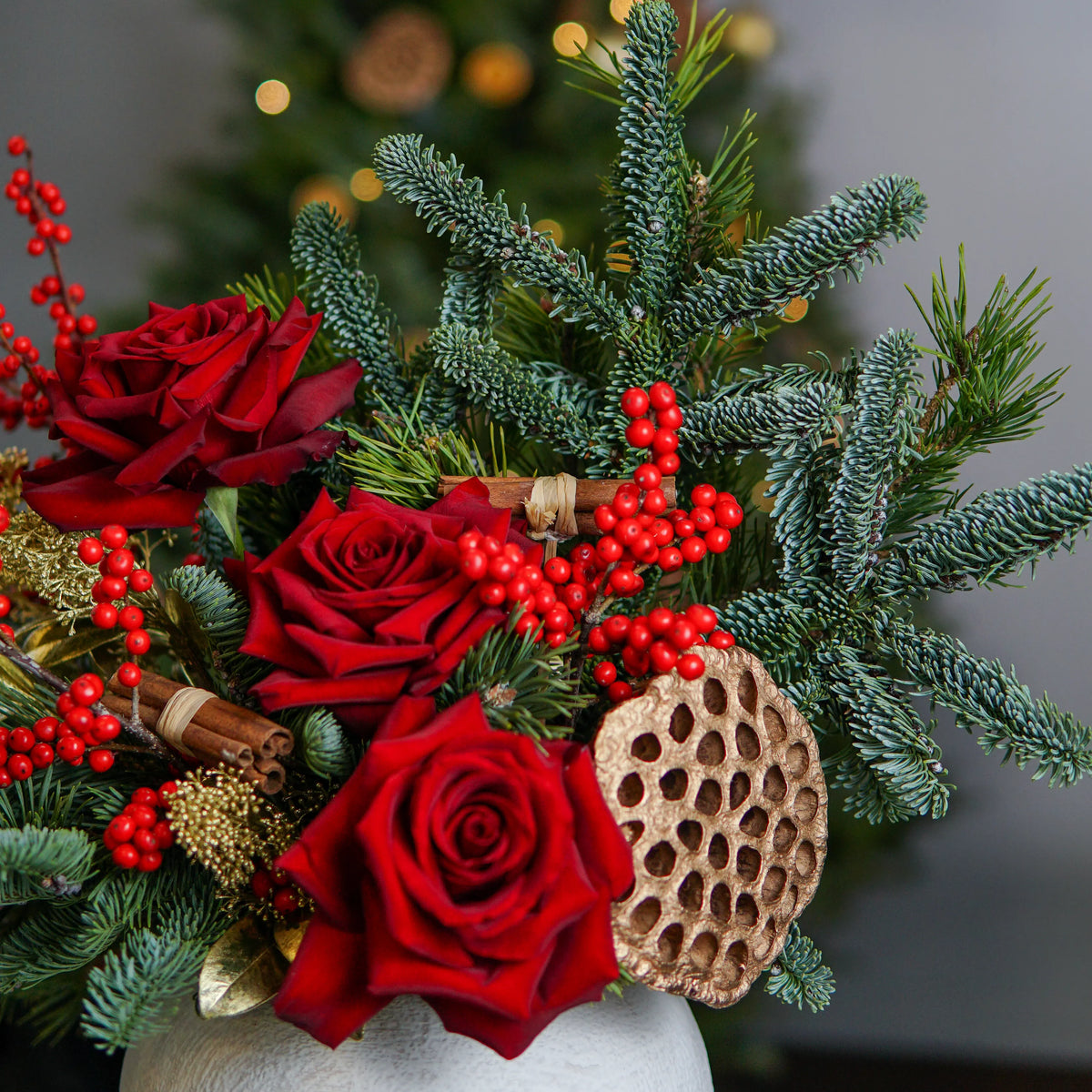 Christmas-themed floral arrangement with red roses, greenery, and a wooden ornament.