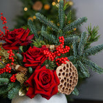 Christmas-themed floral arrangement with red roses, greenery, and a wooden ornament.