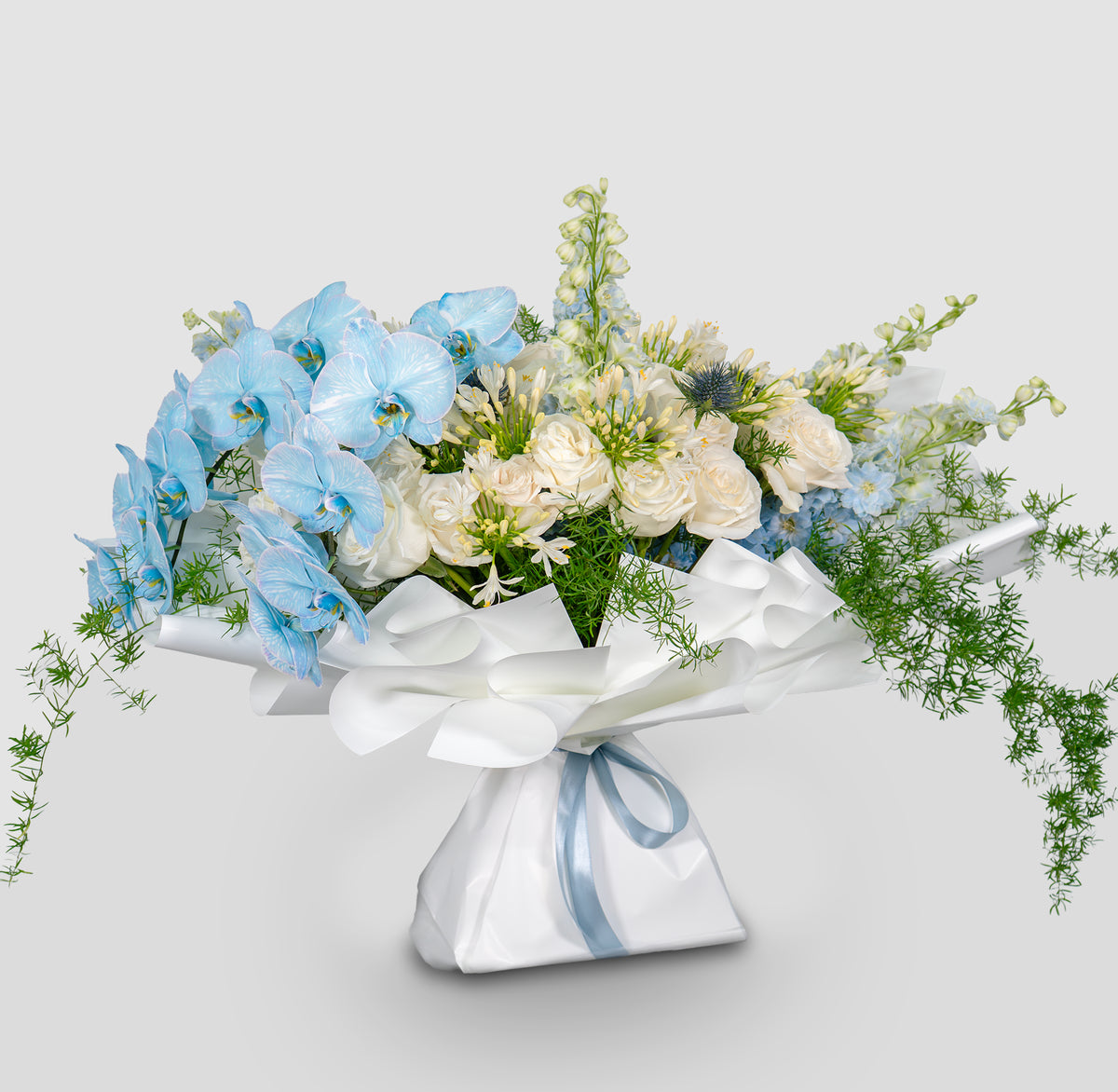 Bouquet of flowers wrapped in white paper with blue ribbons on a light gray background