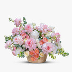 Medium wicker basket with pastel pink roses, peach spray roses, white peonies, cream roses, and green foliage.