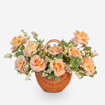 Wicker basket filled with peach-colored roses and greenery on a white background