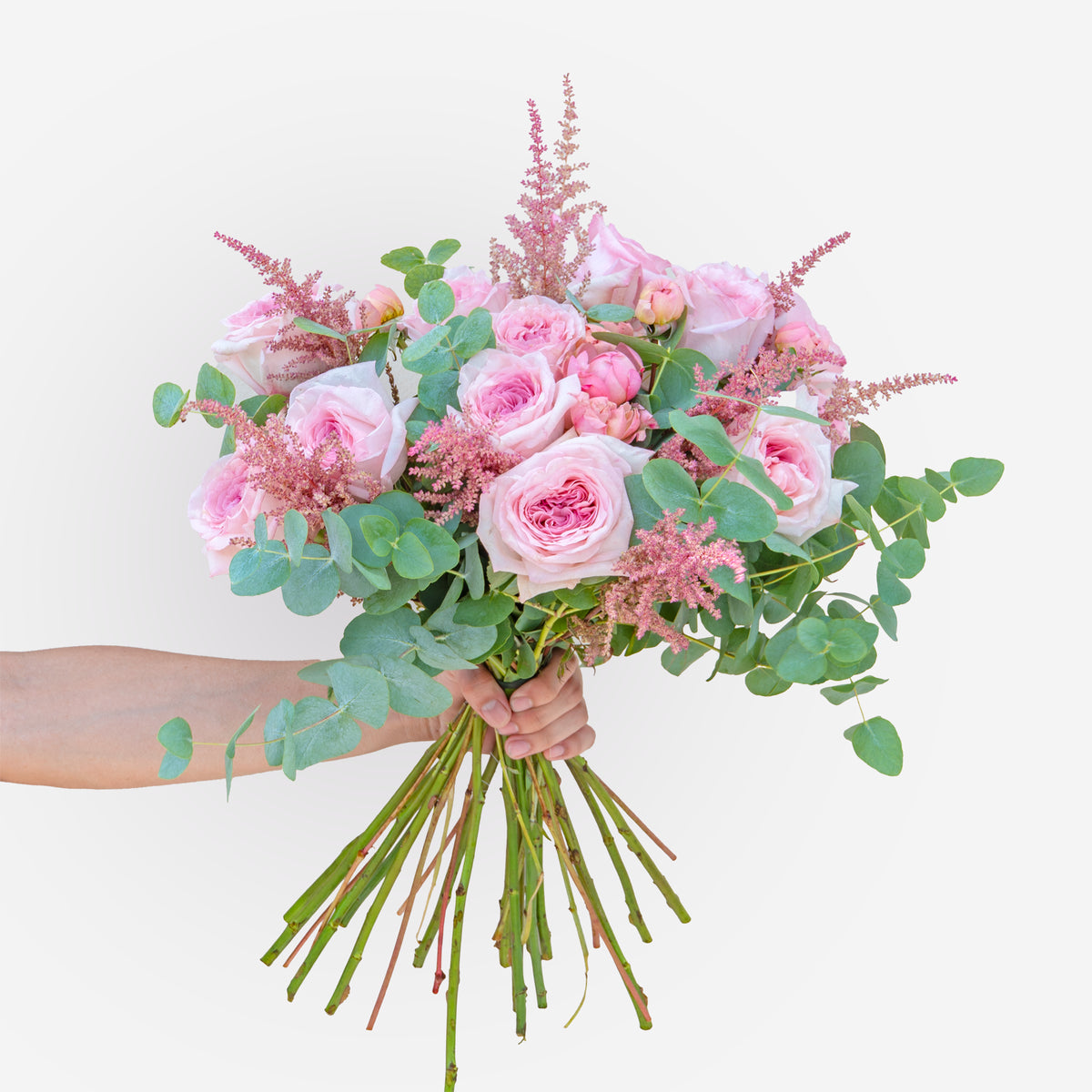 Hand-tied bouquet of soft pink roses with astilbe and eucalyptus, held in hand, fresh flower arrangement available for same-day delivery in Dubai & Sharjah.