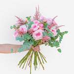 Hand-tied bouquet of soft pink roses with astilbe and eucalyptus, held in hand, fresh flower arrangement available for same-day delivery in Dubai & Sharjah.