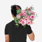 Person holding a large bouquet of pink flowers with greenery on a white background