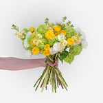 Bouquet of yellow, green, and white flowers held by a hand on a white background