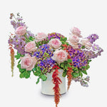Colorful flower arrangement with pink, purple, and green flowers in a white container on a white background