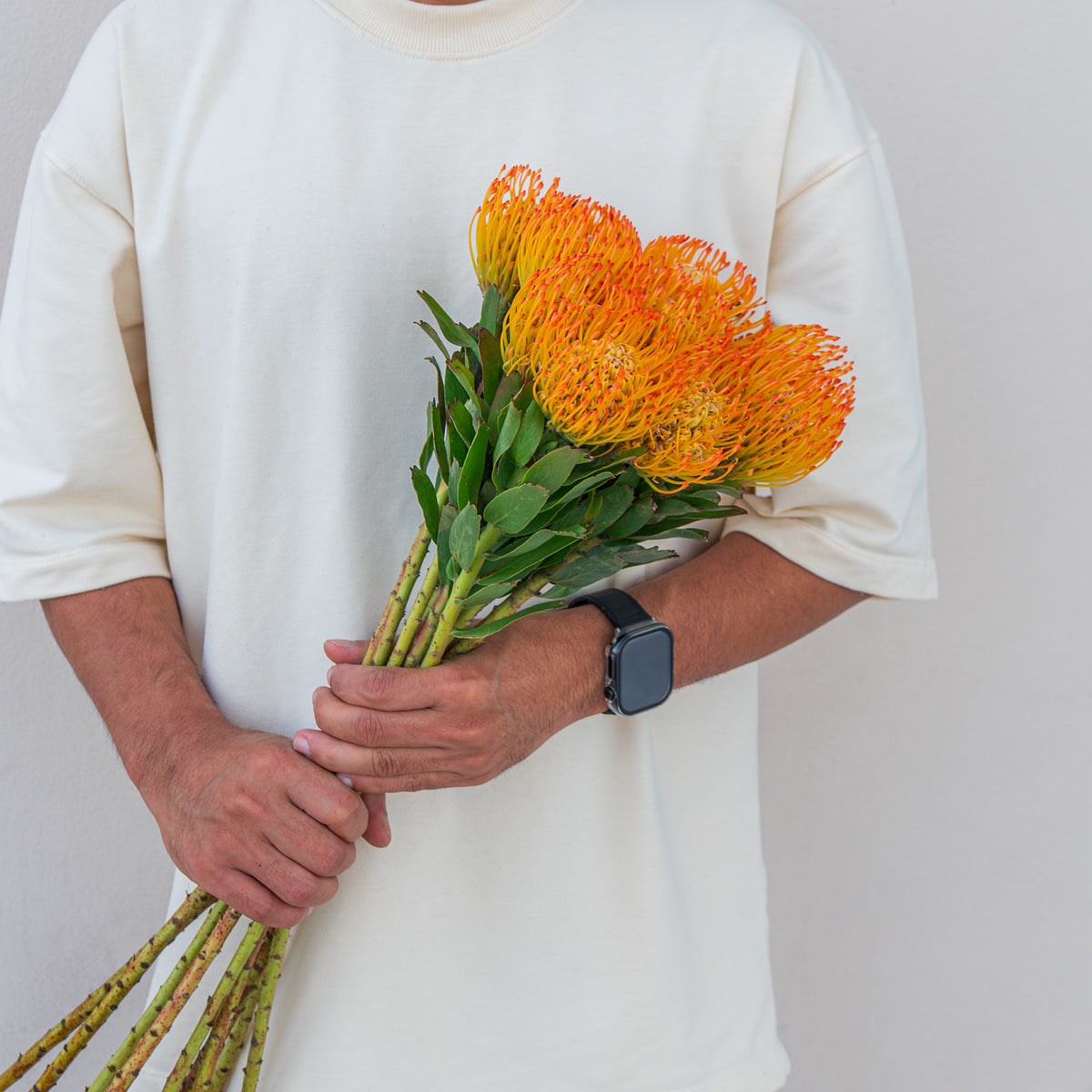 Person holding a bouquet of orange flowers against a plain background