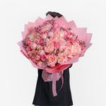 Bouquet of pink and white flowers held by a person wearing a black dress on a white background