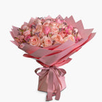 Bouquet of pink roses wrapped in pink paper with a bow on a white background