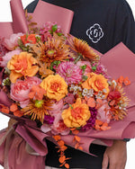 Bouquet of flowers held by a person with a visible brand logo on a white background