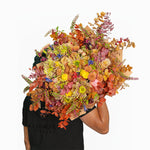 Person holding a large, colorful bouquet of flowers against a white background