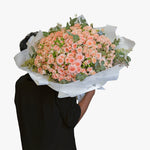 Person holding a large bouquet of pink flowers wrapped in white paper against a white background