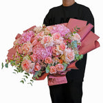 Person holding a bouquet of pink and white flowers with pink paper wrap on a white background