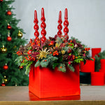 Decorative arrangement with red candles and festive elements on a table, Christmas tree in the background
