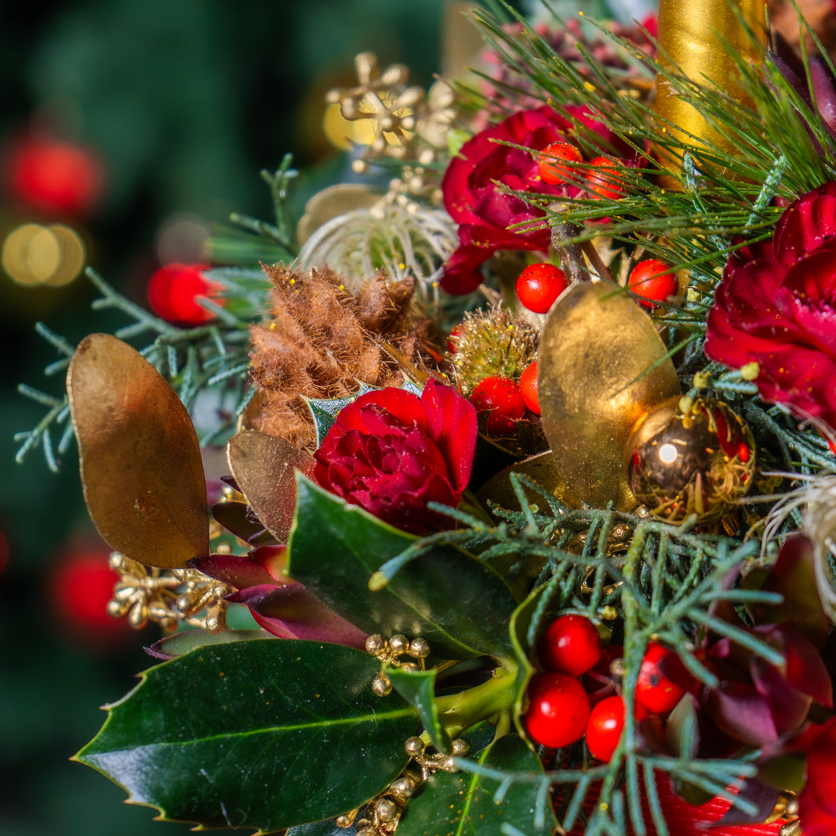 Decorative floral arrangement with red flowers, gold leaves, and greenery on a blurred background