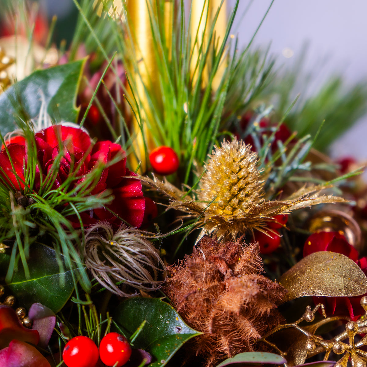 Decorative arrangement with red berries, green leaves, and gold elements on a blurred background