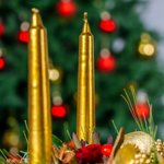Two gold candles with a blurred Christmas tree in the background