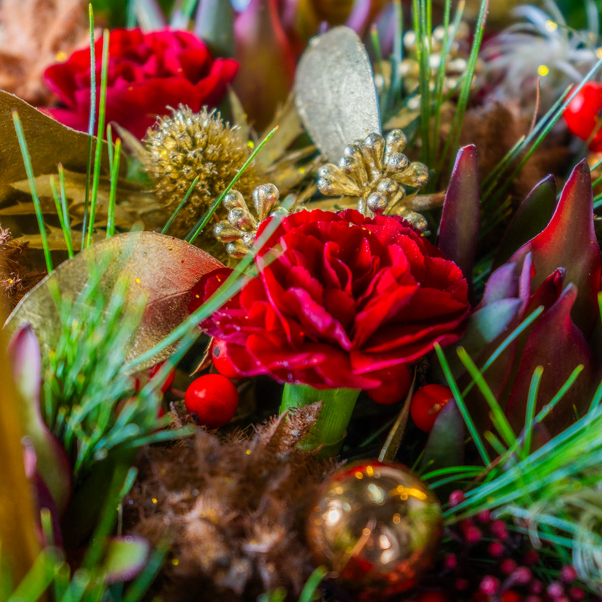 Close-up of a festive floral arrangement with red flowers, gold ornaments, and greenery.