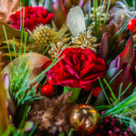 Close-up of a festive floral arrangement with red flowers, gold ornaments, and greenery.