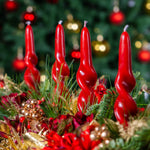 Red candles in a festive arrangement with greenery and ornaments against a blurred Christmas tree background.
