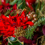 Close-up of a festive flower arrangement with red flowers, gold berries, and greenery.