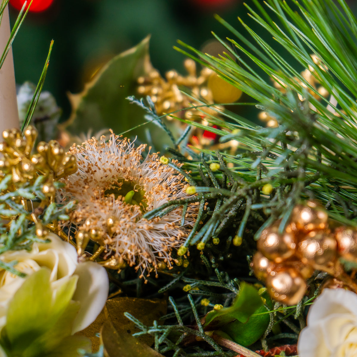 Close-up of a festive arrangement with greenery, gold berries, and white flowers.