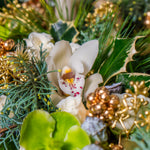 Close-up of a floral arrangement with white orchids, green leaves, and gold accents.