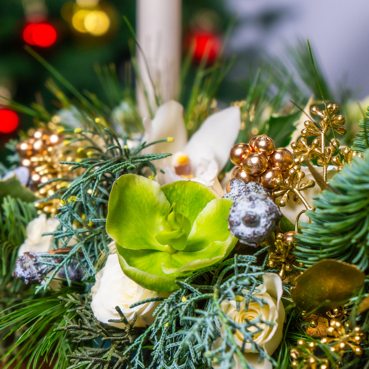 Close-up of a festive floral arrangement with green leaves, gold berries, and white flowers.