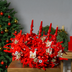 Decorative red wreath with candles and ornaments on a gold stand, Christmas tree in the background.