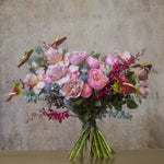 A bouquet of pink, red, and green flowers arranged elegantly against a neutral background.
