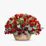 Medium woven basket filled with fresh red roses, spray roses, and eucalyptus, arranged for romantic occasions.