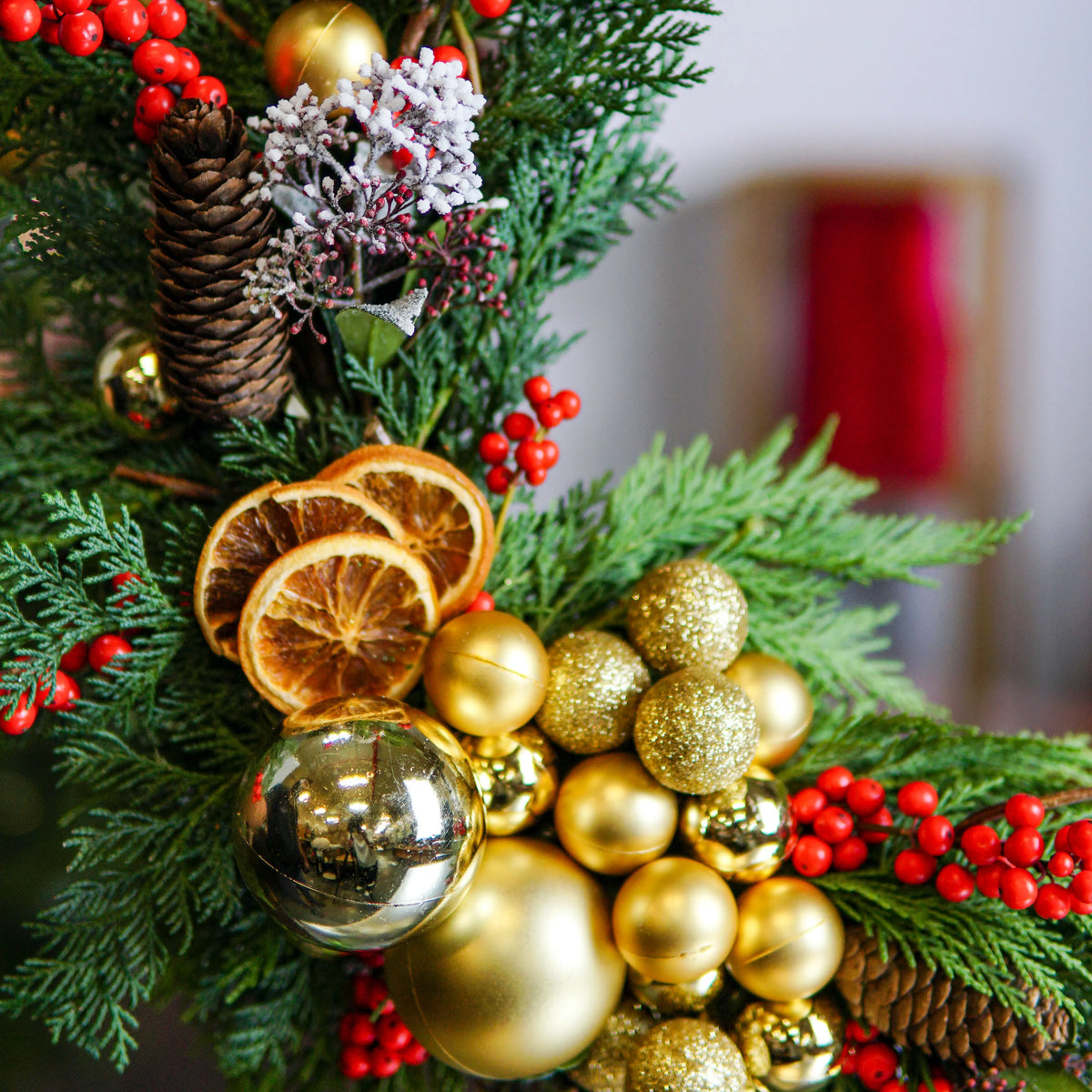 Decorative Christmas wreath with gold ornaments, pine cones, and red berries on a blurred background.