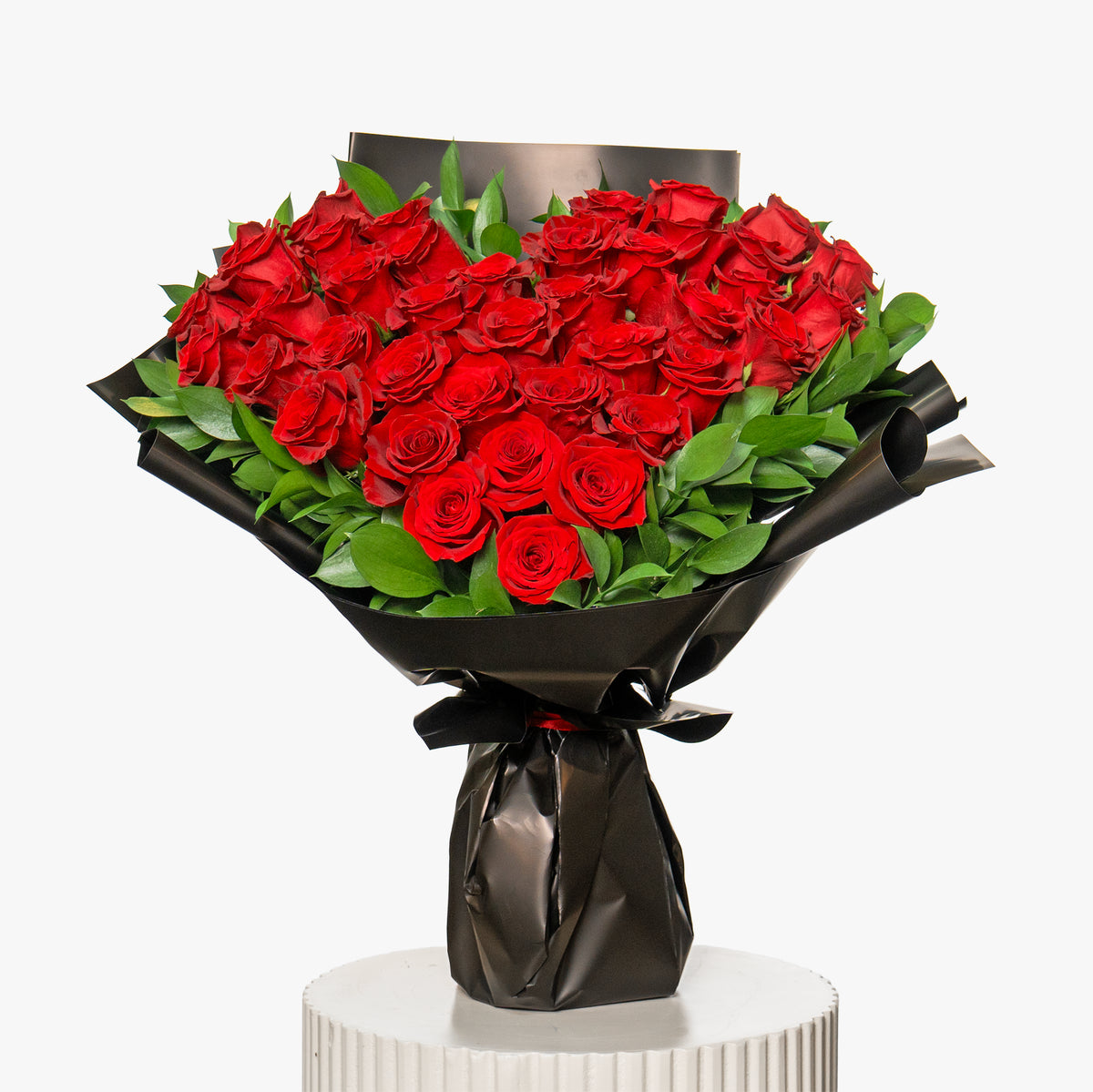 Bouquet of red roses wrapped in black paper on a white pedestal with a white background