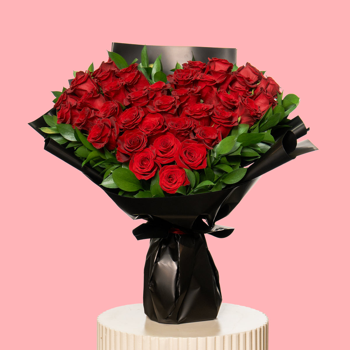 Bouquet of red roses wrapped in black paper on a pink background
