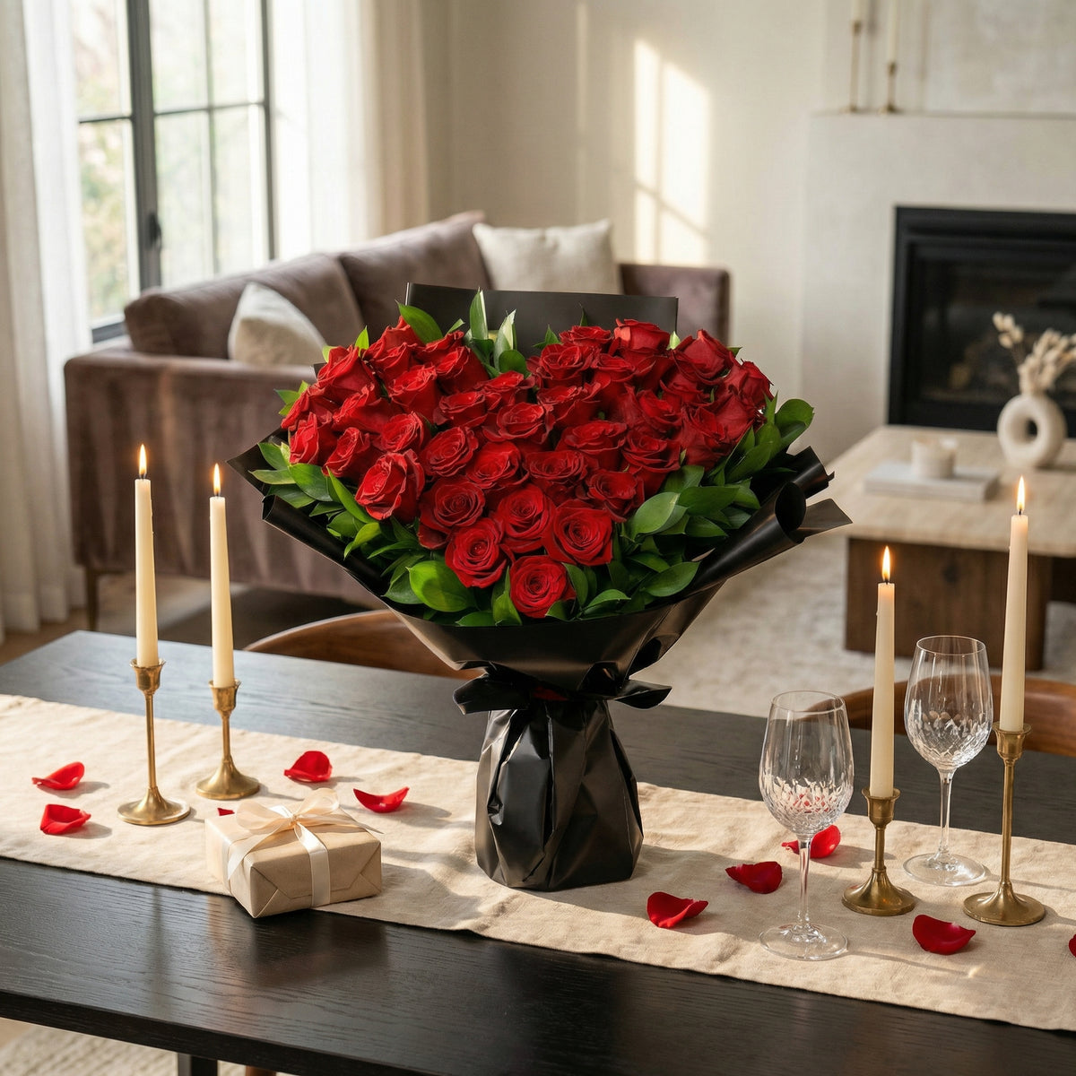 Heart-shaped arrangement of red roses on a table with candles and wine glasses in a living room setting.
